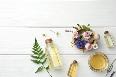 Photo of Aromatherapy. Different essential oils, green twig and flowers on white wooden table, flat lay. Space for text