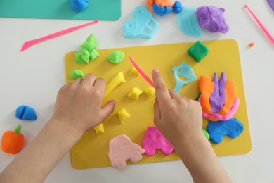 Photo of Little girl sculpting with play dough at white table, top view