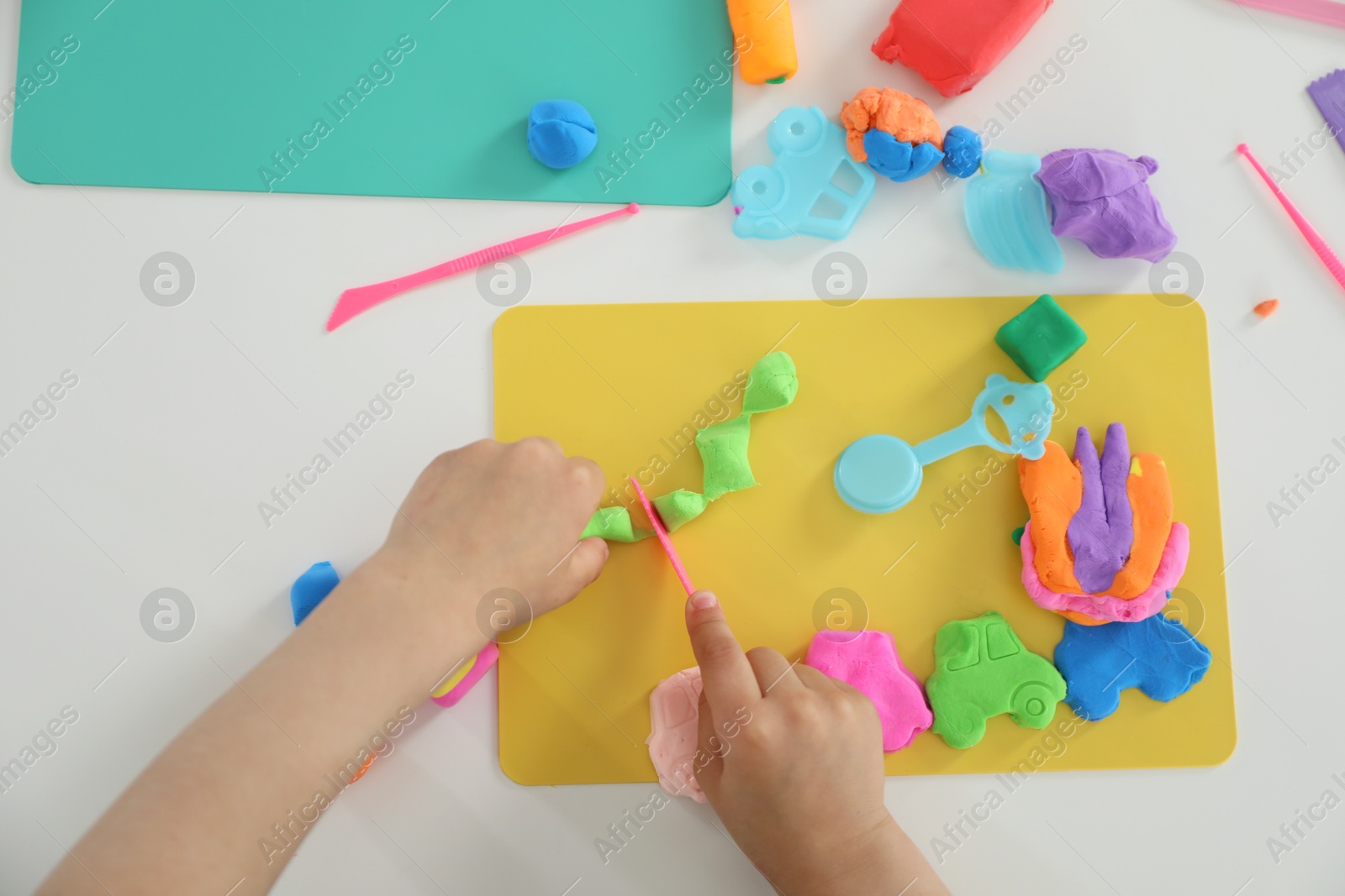 Photo of Little girl sculpting with play dough at white table, top view