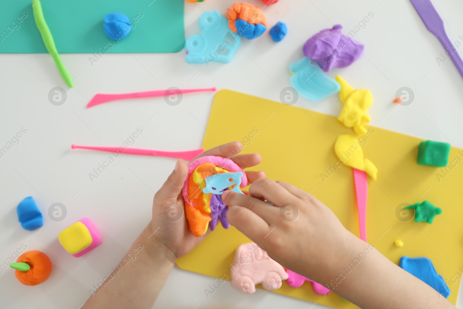 Photo of Little girl sculpting with play dough at white table, top view