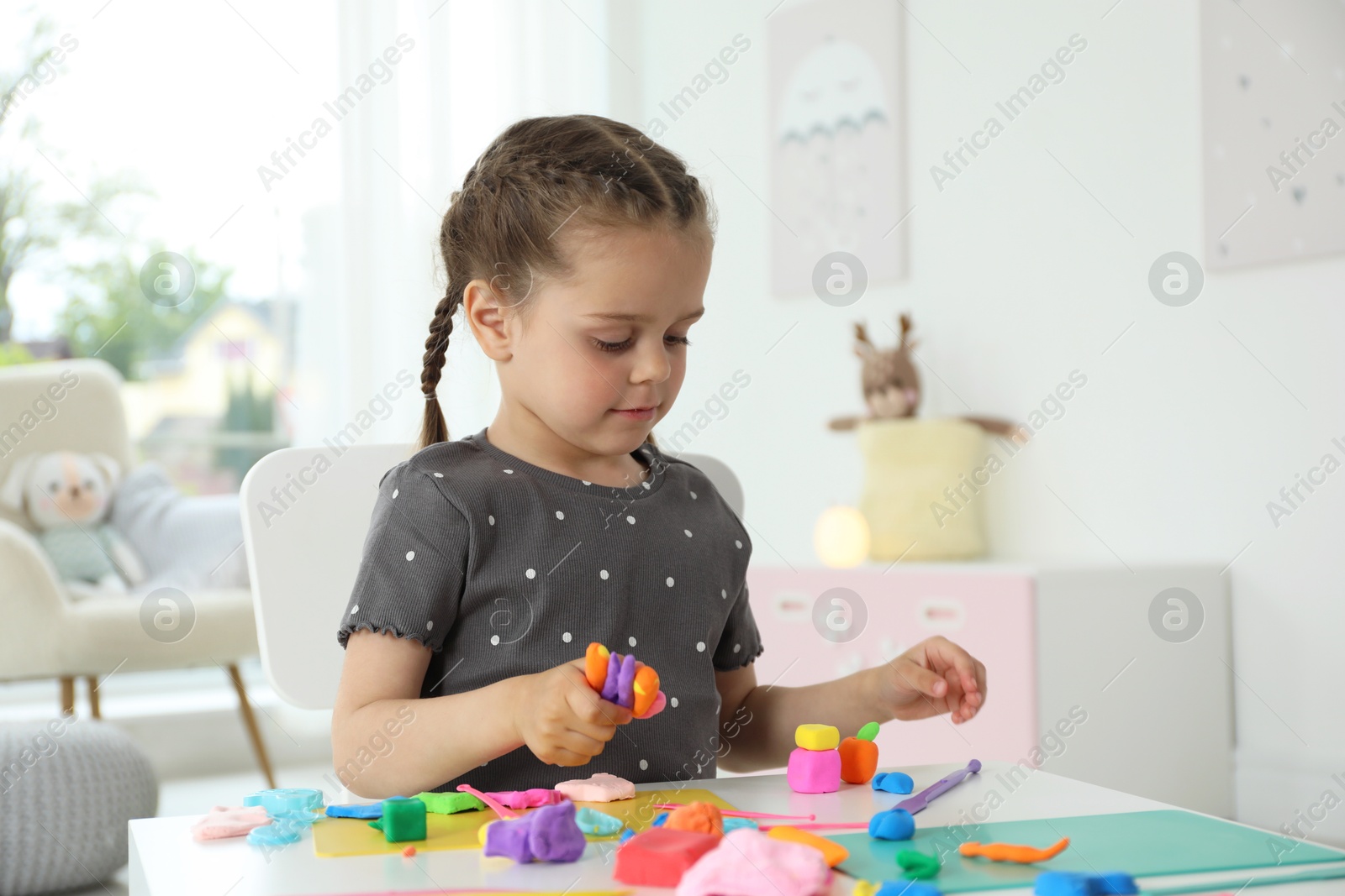 Photo of Little girl sculpting with play dough at table in kindergarten