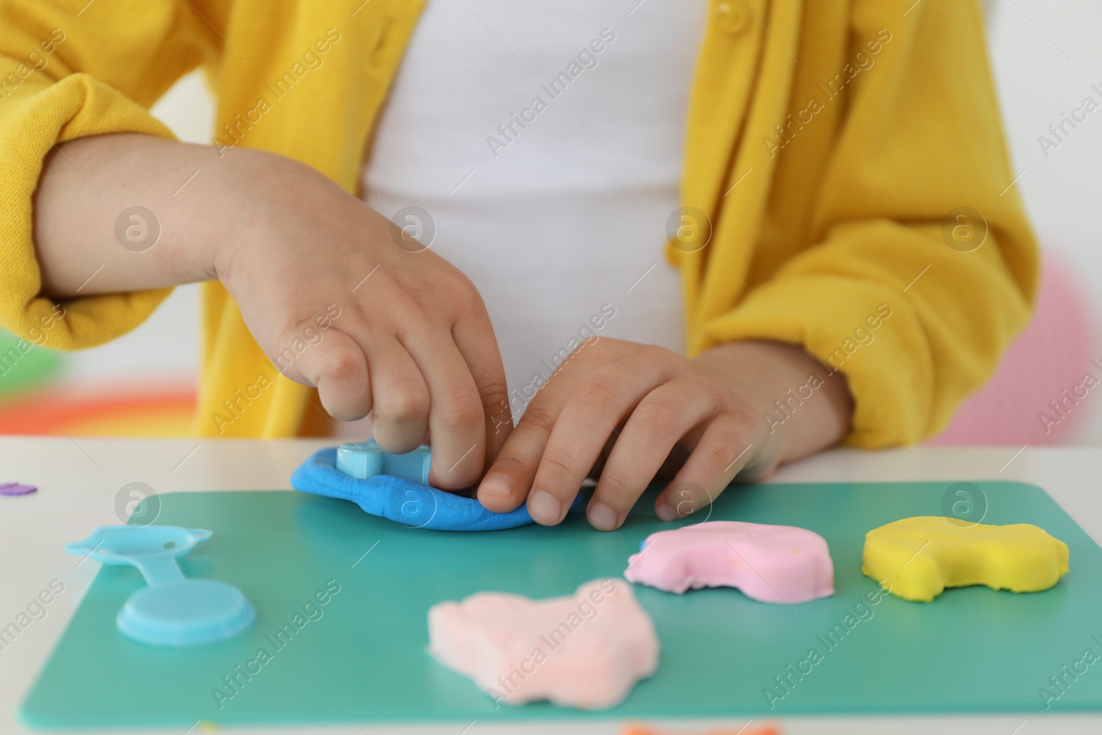 Photo of Little girl sculpting with play dough at table indoors, closeup