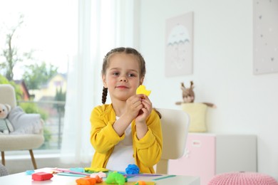 Photo of Little girl sculpting with play dough at table in kindergarten