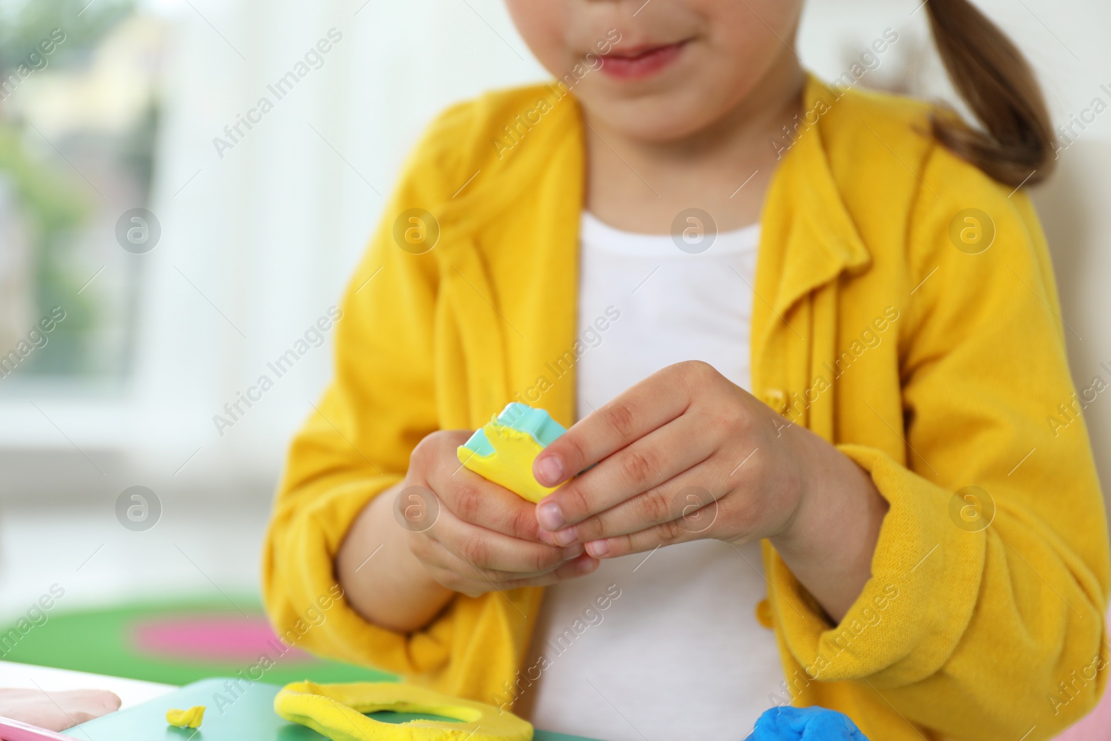 Photo of Little girl sculpting with play dough at home, closeup