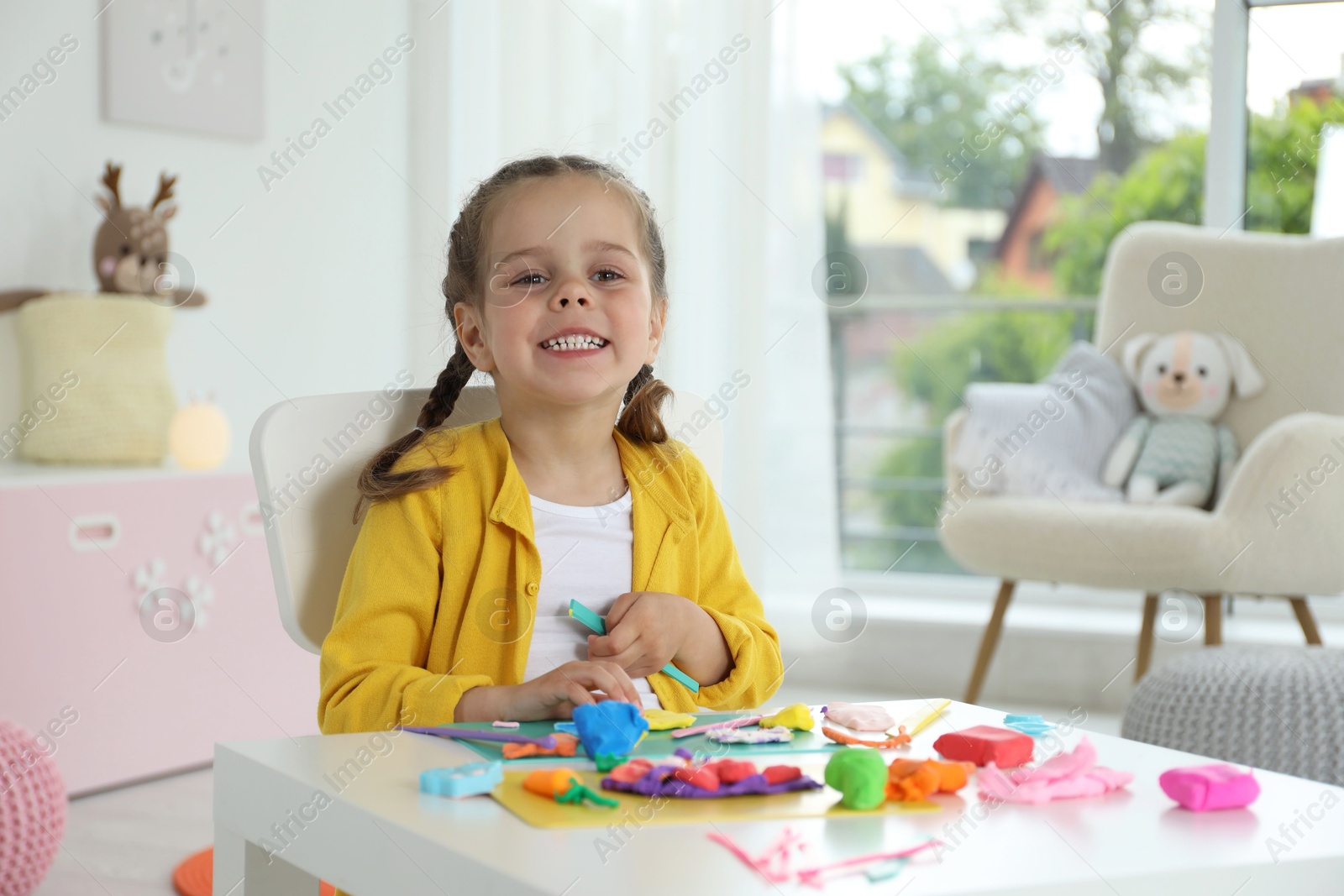 Photo of Happy girl with play dough at table in kindergarten