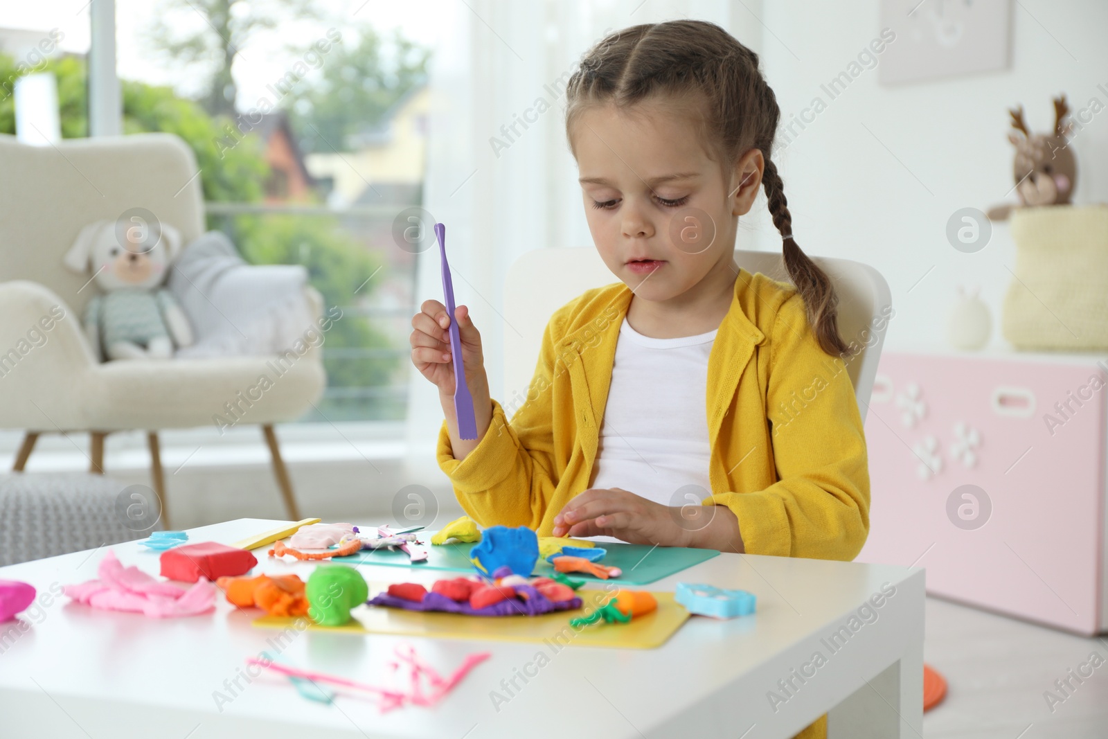 Photo of Little girl sculpting with play dough at table in kindergarten