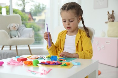 Photo of Little girl sculpting with play dough at table in kindergarten