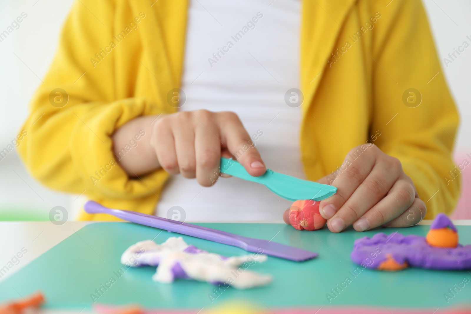 Photo of Little girl sculpting with play dough at table indoors, closeup