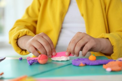 Photo of Little girl sculpting with play dough at table indoors, closeup