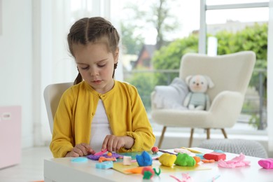 Photo of Little girl sculpting with play dough at table in kindergarten