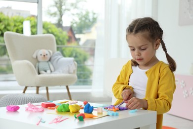 Little girl sculpting with play dough at table in kindergarten