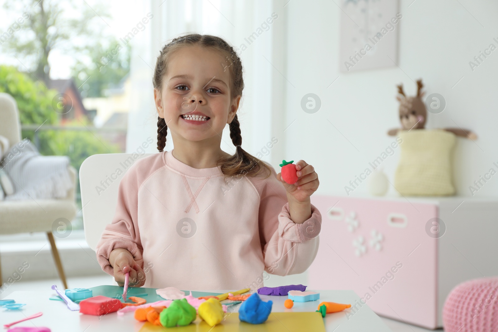 Photo of Smiling girl showing strawberry made from play dough in kindergarten