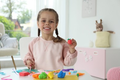 Smiling girl showing strawberry made from play dough in kindergarten