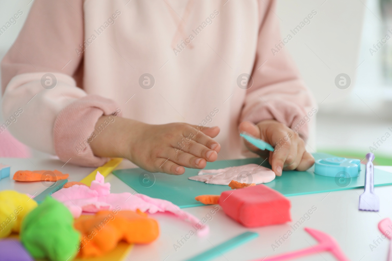 Photo of Little girl sculpting with play dough at table indoors, closeup