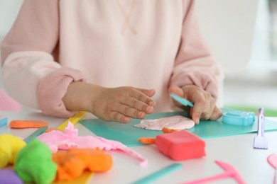 Photo of Little girl sculpting with play dough at table indoors, closeup