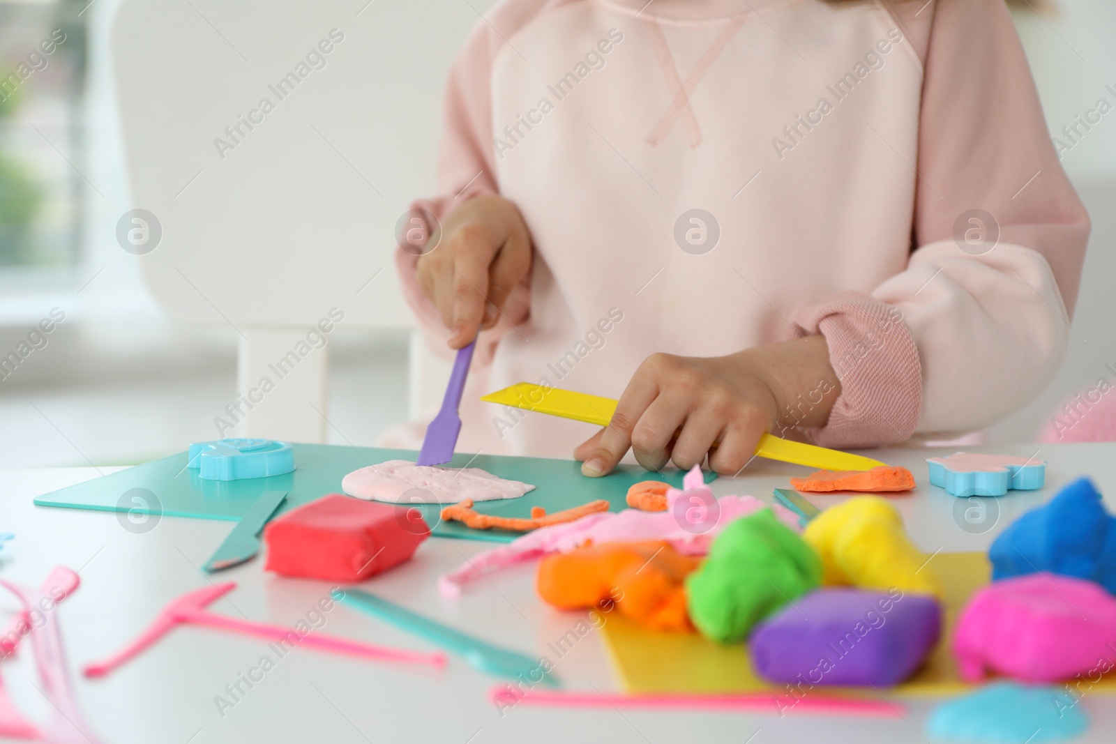 Photo of Little girl sculpting with play dough at table indoors, closeup