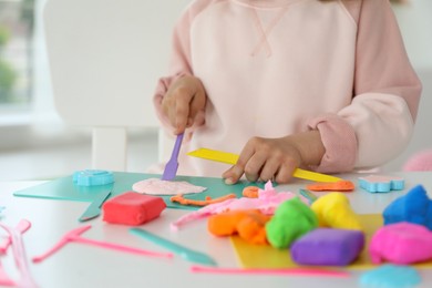 Little girl sculpting with play dough at table indoors, closeup