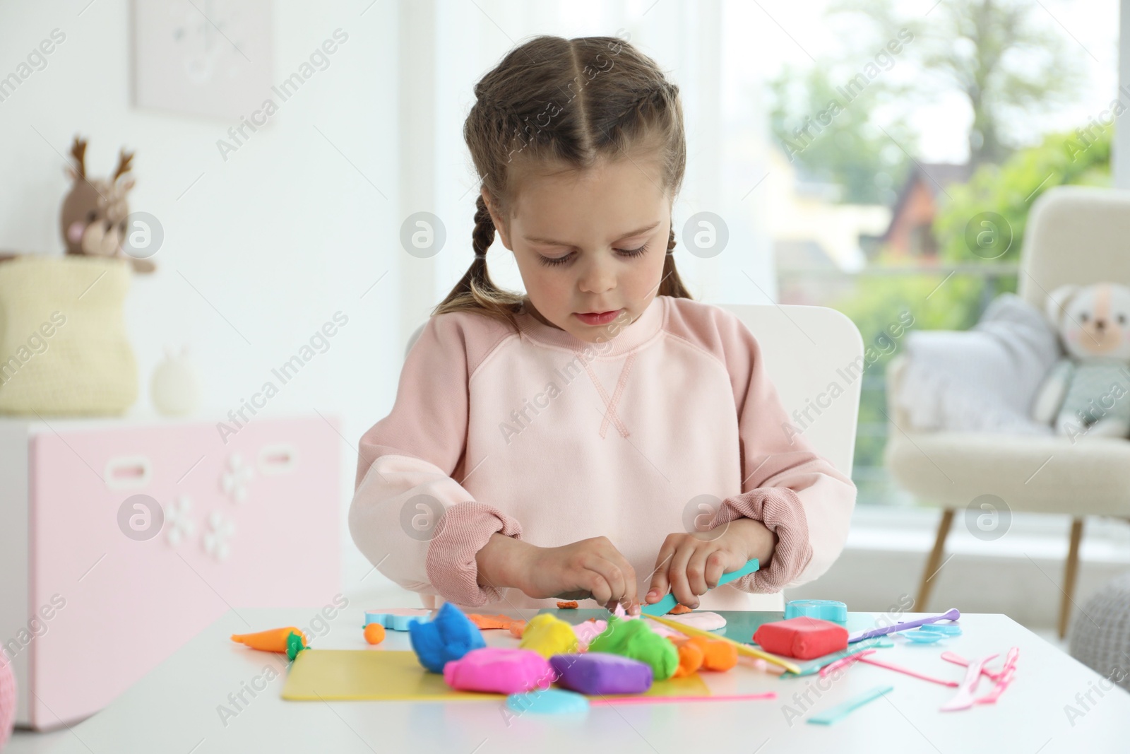 Photo of Little girl sculpting with play dough at table in kindergarten