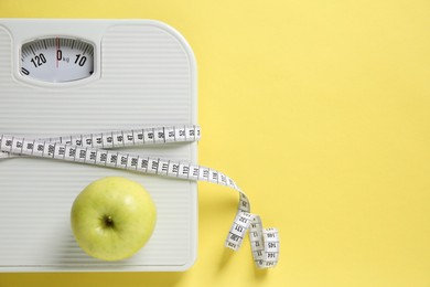 Photo of Scale tied with measuring tape and fresh apple on yellow background, top view. Space for text