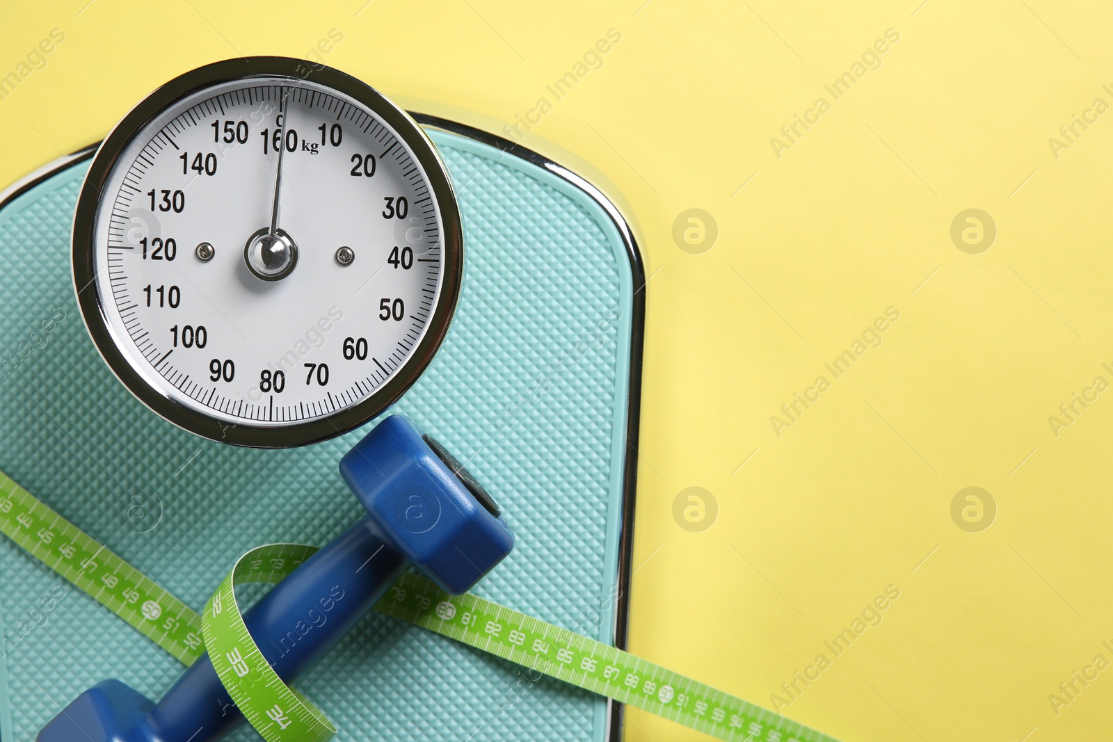 Photo of Scale, measuring tape and dumbbells on yellow background, top view. Space for text