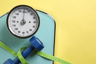 Photo of Scale, measuring tape and dumbbells on yellow background, top view. Space for text