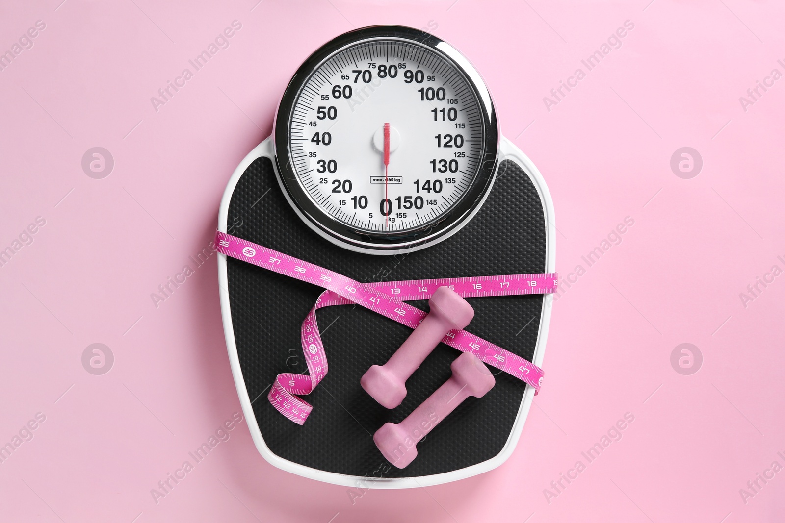 Photo of Scale tied with measuring tape and dumbbells on pink background, top view