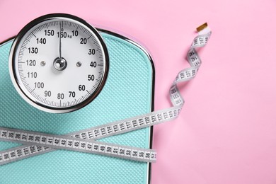 Photo of Scale tied with measuring tape on pink background, top view. Space for text