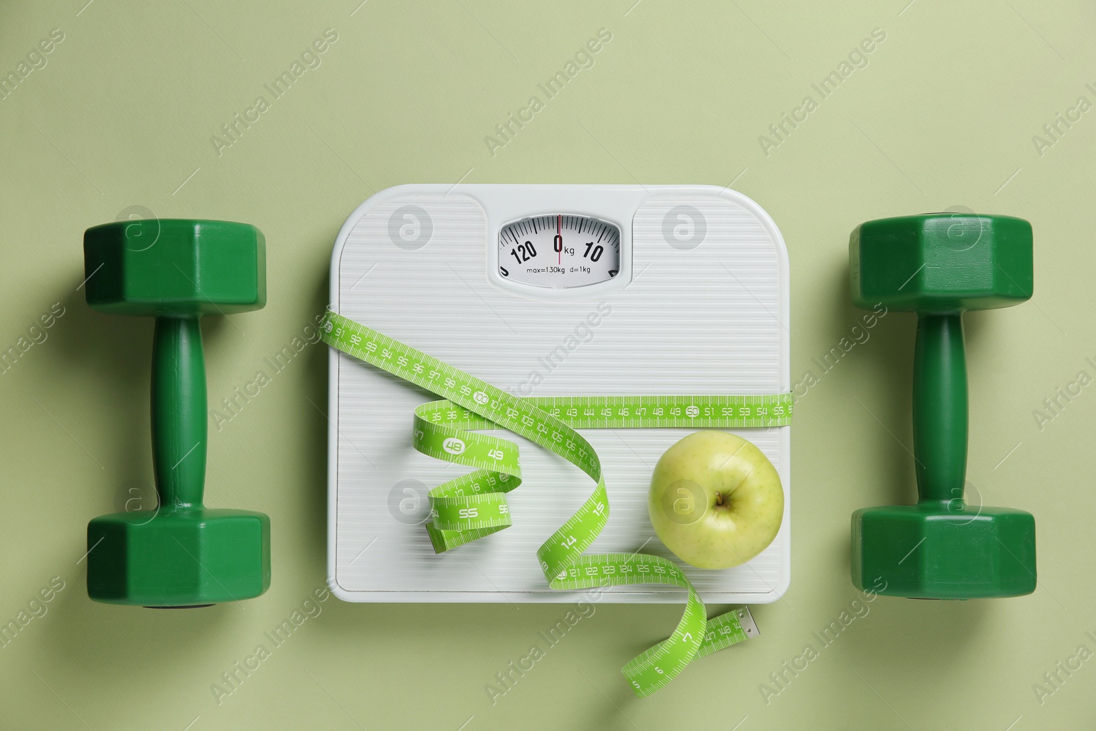 Photo of Scale, measuring tape, dumbbells and fresh apple on olive background, flat lay