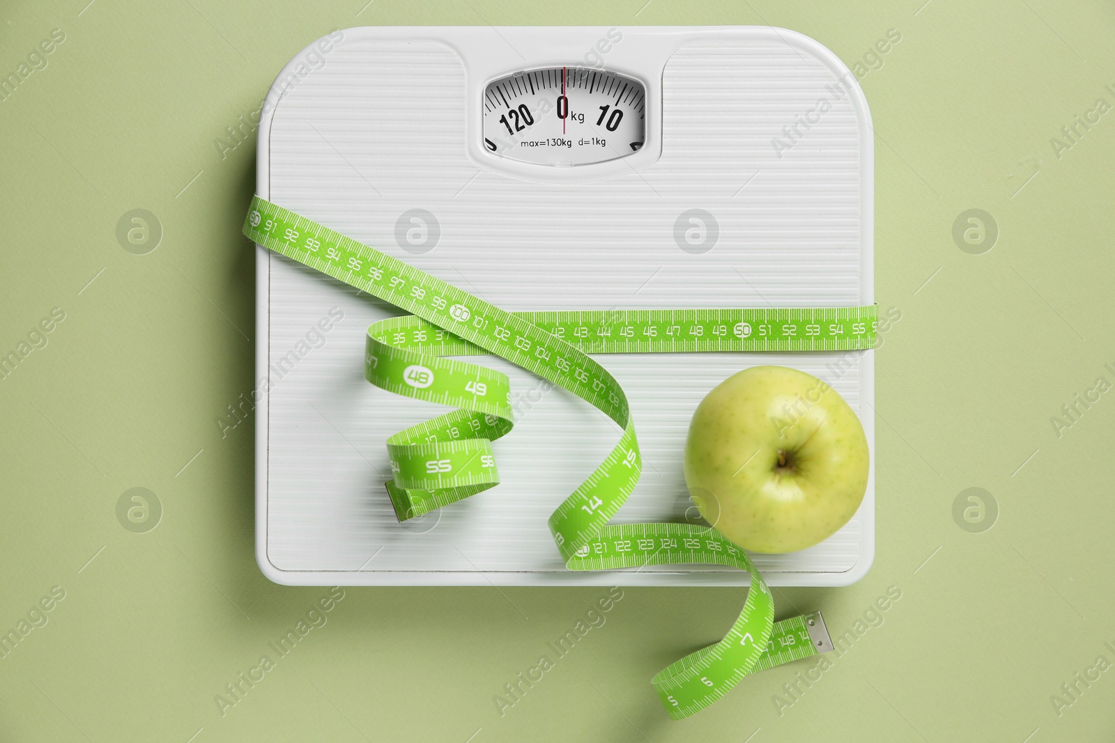 Photo of Scale tied with measuring tape and fresh apple on olive background, top view