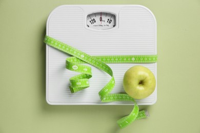 Photo of Scale tied with measuring tape and fresh apple on olive background, top view