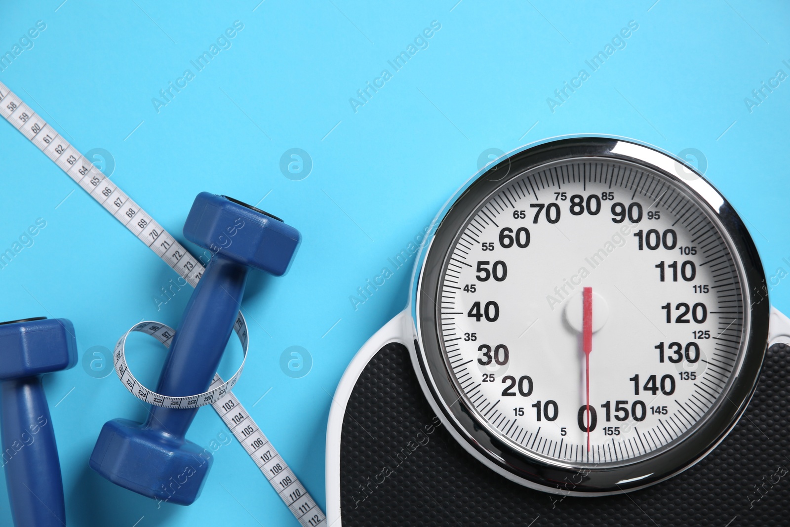 Photo of Scale, dumbbells and measuring tape on light blue background, flat lay