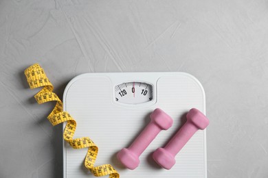 Photo of Bathroom scale, measuring tape and dumbbells on grey textured background, flat lay