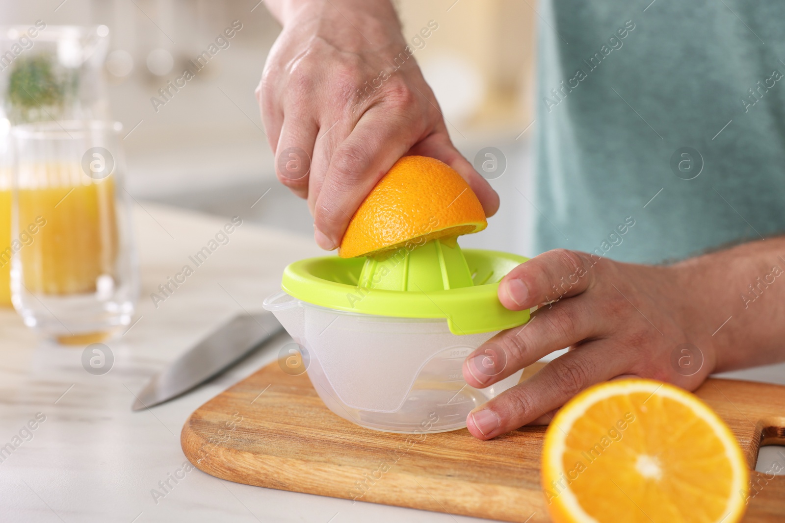 Photo of Man squeezing fresh orange with juicer at white table in kitchen, closeup