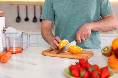 Photo of Making juice. Man cutting fresh orange at white marble table in kitchen, closeup