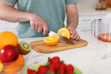Photo of Making juice. Man cutting fresh orange at white marble table in kitchen, closeup