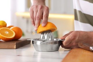 Photo of Man squeezing fresh orange with juicer at white marble table, closeup