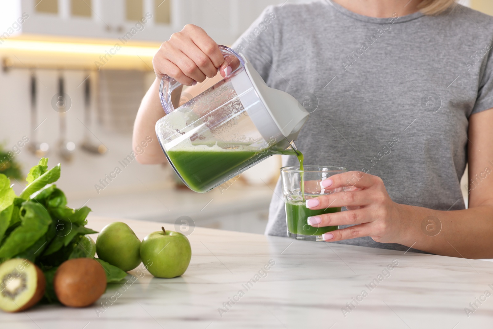 Photo of Woman pouring fresh juice into glass at white marble table in kitchen, closeup