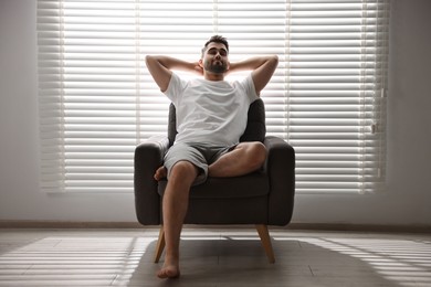 Photo of Man sitting on armchair near window blinds indoors