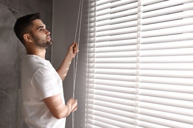 Photo of Man adjusting window blinds at home, space for text