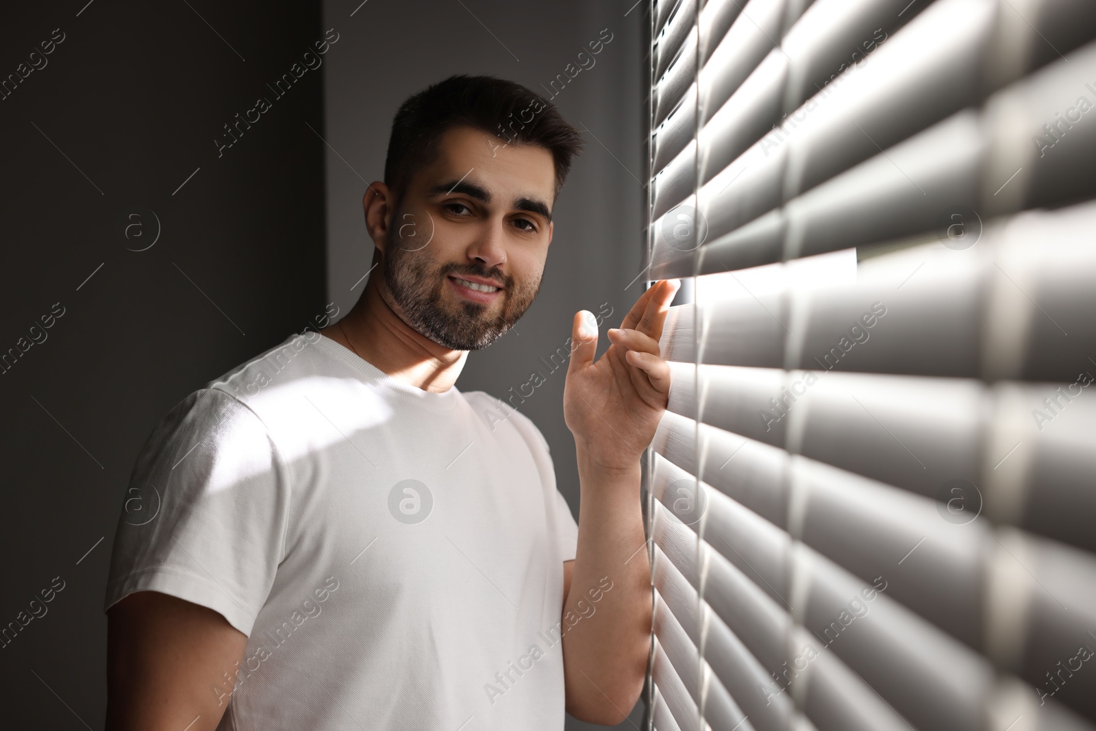 Photo of Man near window blinds at home, space for text