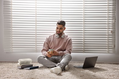Photo of Man with laptop and books sitting near window blinds at home