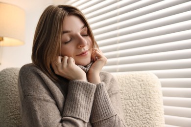 Photo of Woman sitting on armchair near window blinds at home, space for text