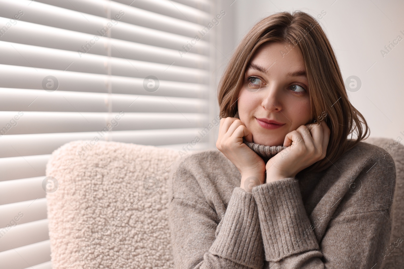 Photo of Woman sitting on armchair near window blinds at home, space for text