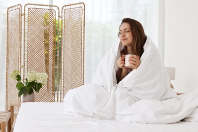 Bedtime. Woman wrapped in blanket holding cup of drink on bed indoors