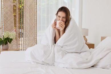 Bedtime. Woman wrapped in blanket holding cup of drink on bed indoors