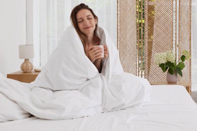 Bedtime. Woman wrapped in blanket holding cup of drink on bed indoors