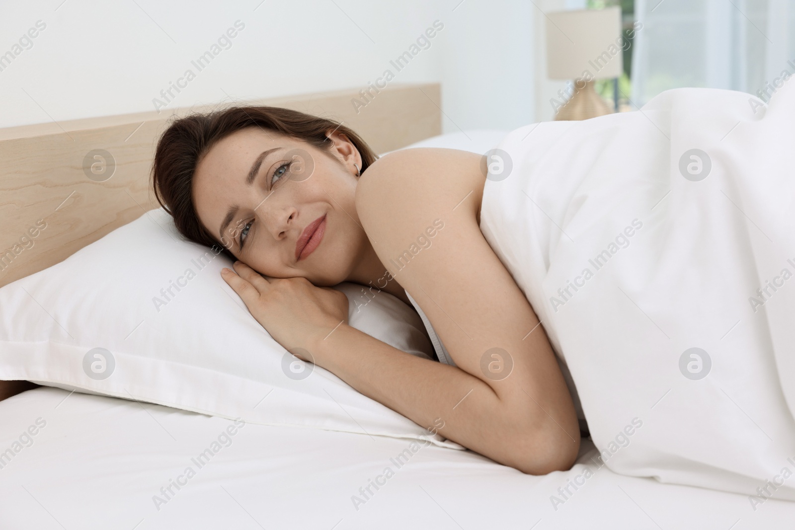 Photo of Bedtime. Smiling woman lying in bed indoors