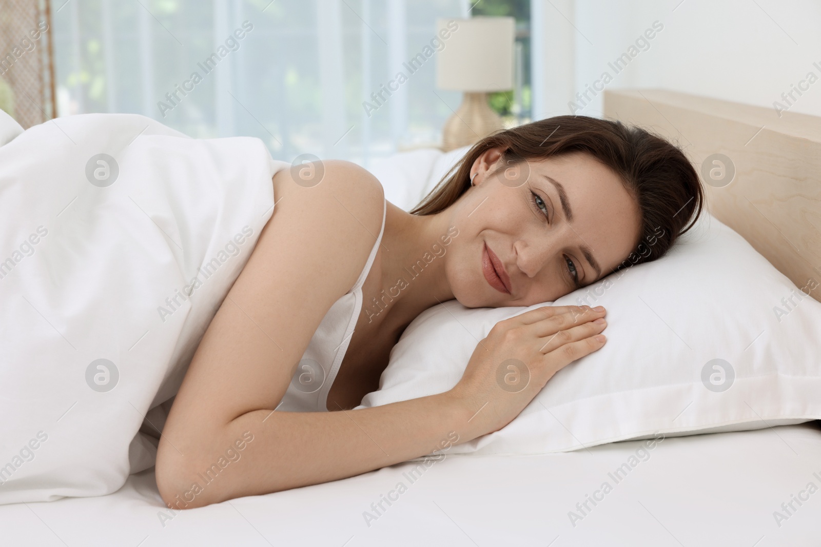 Photo of Bedtime. Smiling woman lying in bed indoors