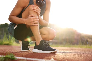 Sportsman with leg injury suffering from knee pain at stadium, closeup. Space for text