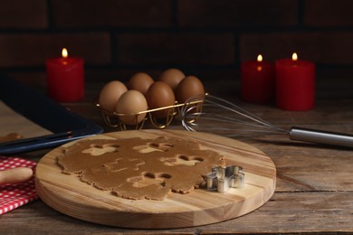 Photo of Raw dough, cookie cutter, whisk, eggs and burning candles on wooden table